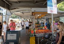 TikTok-Trend Wochenmarkt Der Markt mit Obstständen unter der U-Bahn Brücke. Einige Menschen laufen umher. Das Schild zeigt die Aufschrift Isemarkt.