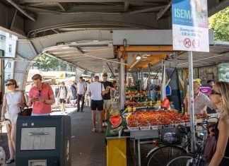 TikTok-Trend Wochenmarkt Der Markt mit Obstständen unter der U-Bahn Brücke. Einige Menschen laufen umher. Das Schild zeigt die Aufschrift Isemarkt.