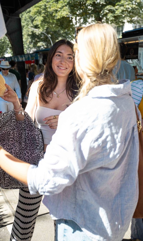 Eine junge Frau lächelt ihre Freundin an, die mit dem Rücken zur Kamera steht. Die beiden stehen an einem Cardigan-Stand.