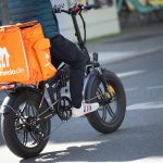 Warnstreik bei Lieferando Eine Person sitzt auf einem Fahrrad. Auf dem Gepäckträger ist eine orangefarbene Thermobox mit dem Lieferando-Logo befestigt.