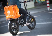 Warnstreik bei Lieferando Eine Person sitzt auf einem Fahrrad. Auf dem Gepäckträger ist eine orangefarbene Thermobox mit dem Lieferando-Logo befestigt.