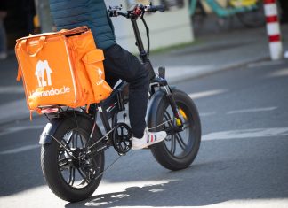 Warnstreik bei Lieferando Eine Person sitzt auf einem Fahrrad. Auf dem Gepäckträger ist eine orangefarbene Thermobox mit dem Lieferando-Logo befestigt.