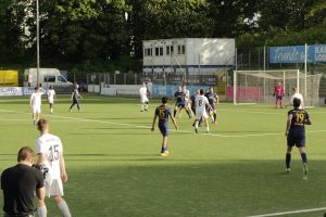 Mehrere Spieler stehen eng beieinander im und rund um den Strafraum, im linken Vordergrund bedient jemand am Spielfeldrand eine