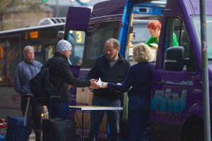 Zu sehen sind mehrere Menschen vor dem Mitternachtsbus. Ehrenamtliche Helfer*innen stehen am Bus und geben obdachlosen Menschen etwas zu Essen.