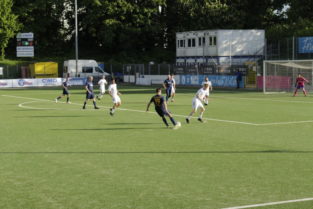 Zehn Fußballer in einer Spielszene. Einer schlägt eine Flanke, die anderen stehen herum.
