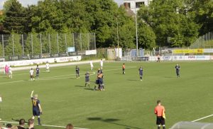 Mehrere Spieler liegen sich beim Torjubel in den Armen. Im Vordergrund links reckt ein Ersatzspieler jubelnd den linken Arm in die Luft, rechts macht sich der Linienrichter Notizen.