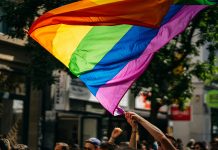 Queere Sichtbarkeit: Ein gar nicht mal so lustiger „Zirkus“ ein Mensch schwenkt eine Regenbogenflagge auf einer Demonstration für mehr queere Sichtbarkeit