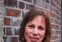 Sexualbegleiterin Bianka Pille Ein Porträt von Bianka Pille. Sie lehnt an einer Backsteinwand und schaut lächelnd in die Kamera. Sie trägt ein weinrotes Oberteil.