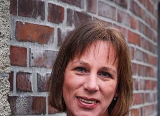 Sexualbegleiterin Bianka Pille Ein Porträt von Bianka Pille. Sie lehnt an einer Backsteinwand und schaut lächelnd in die Kamera. Sie trägt ein weinrotes Oberteil.