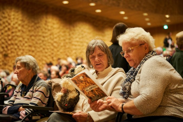 Mehrere ältere Frauen sitzen in einem Konzertsaal. Zwei ältere Frauen mit weißen und grauen Haaren halten ein Liederheft in ihren Händen. Sie besuchen ein Klangzeitkonzert in der Elbphilharmonie.