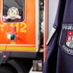 Brand in Flüchtlingsunterkunft: Vier Verletzte Ein Feuerwehrauto mit einer Person in einer Feuerschutzjacke im Vordergrund symbolisiert den Feuereinsatz in der Flüchtlingsunterkunft. Symbolbild für den Brand und dem Einsatz der Feuerwehr.