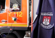 Brand in Flüchtlingsunterkunft: Vier Verletzte Ein Feuerwehrauto mit einer Person in einer Feuerschutzjacke im Vordergrund symbolisiert den Feuereinsatz in der Flüchtlingsunterkunft. Symbolbild für den Brand und dem Einsatz der Feuerwehr.