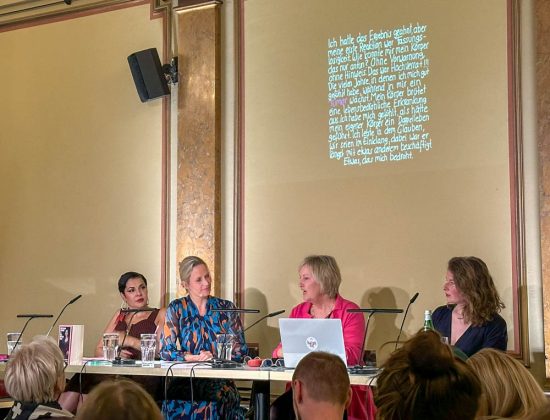 Vier Frauen sitzen auf der Bühne in einem Saal.