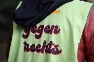 Man sieht den Rücken eines Demonstrationsteilnehmer, der eine gelbe Weste mit der Aufschrift: "gegen rechts" trägt.
