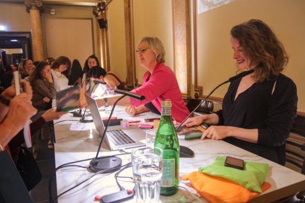 Zwei Frauen sitzen an einem Tisch und unterhalten sich mit Besuchenden.