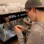 Mittendrin statt am Rande der Gesellschaft Eine Frau mit einer Kappe bedient eine Kaffeemaschine.