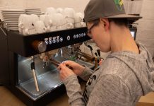 Mittendrin statt am Rande der Gesellschaft Eine Frau mit einer Kappe bedient eine Kaffeemaschine.