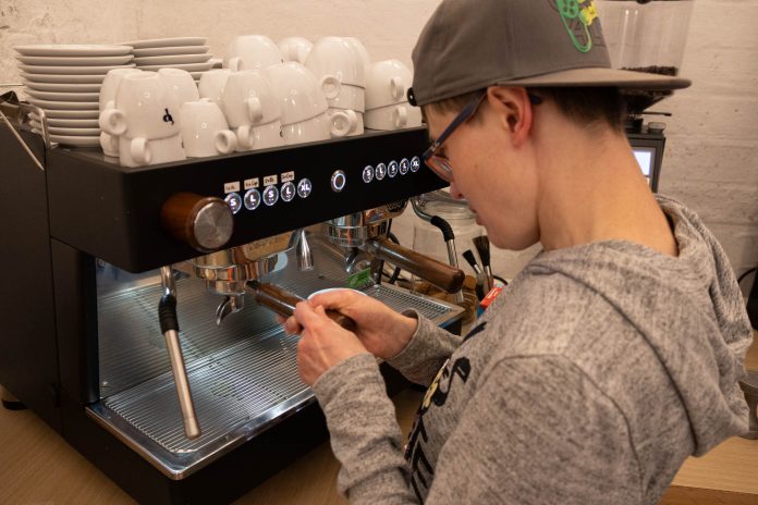 Kaffeemaschine Caroline Eine Frau mit einer Kappe bedient eine Kaffeemaschine.