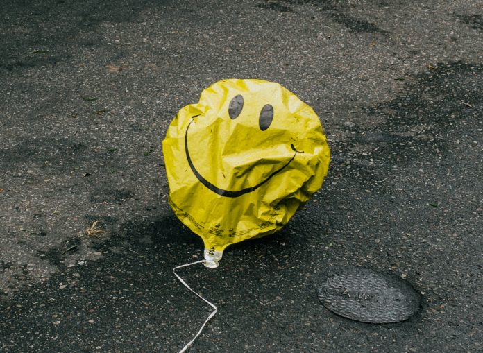 Titelbild Ein zerknitterter gelber Luftballon mit einem Smilely liegt auf der Straße