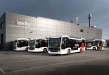 Verkehrsbetriebe Hamburg-Holstein testen Doppeldeckerbus Elektrobusse von vhh.mobility auf dem Betriebshof Bergedorf stehen vor einer gruaen Halle mit der Aufschrift "elexitxy". Die Busflotte wird aktuell durch eine Testphase eines Doppeldeckerbusses erweitert.