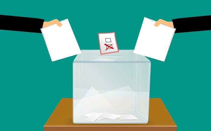 Eine Wahlurne mit zwei Händen in die Wahlzettel reingeworfen werden.