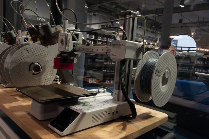 Ein 3D-Drucker steht auf einem Tisch vor einer Glaswand.