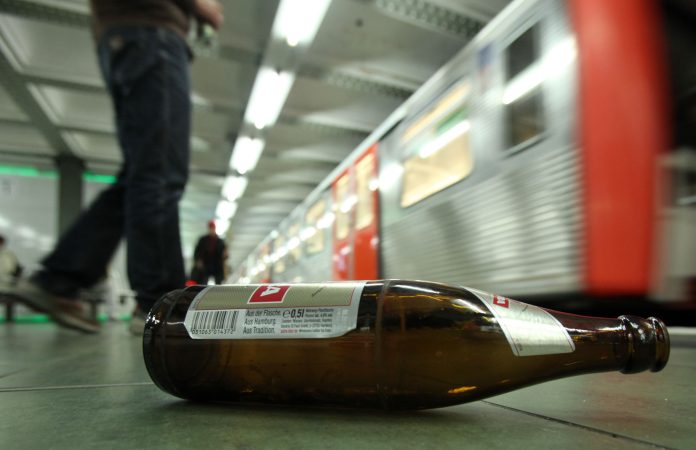 Auf einem Bahnsteig liegt eine leere Bierflasche. Eine U-Bahn fährt gerade ein. Symbolbild: Alkoholkonsumverbot