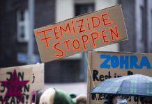 Häusliche Gewalt in Hamburg nimmt zu: Die Opfer sind Frauen Ein braunes Schild wird über den Köpfen von Menschen hochgehalten. darauf steht der orangefarbener Satz "Femizide stoppen"