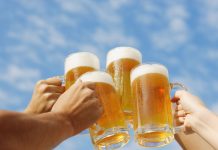 Steigen die Bierpreise? Vie Menschen Stoßen mit vollen Bierkrügen vor einem blauen Himmel an.