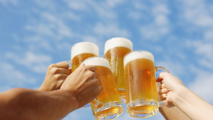 Vie Menschen Stoßen mit vollen Bierkrügen vor einem blauen Himmel an.