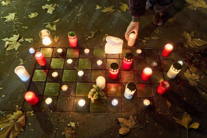 Angezündete rote Kerzen und Blumen stehen am Gedenktag an die Pogromnacht neben Stolpersteinen.