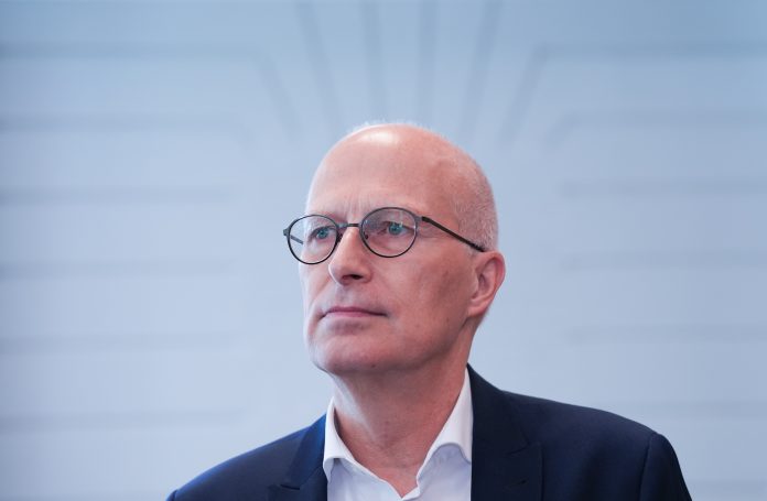 Hamburgs Bürgermeister Peter Tschentscher sitzt vor einem hellen Hintergund und schaut zur Seite.