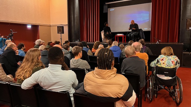 Ein Publikum sitzt im Kinosaal beim Afrikanischen Filmfestival. Die Leinwand ist zu sehen, auf der Bühne sitzen zwei Menschen mit Mikrofon.