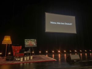 Bühnenbild von Tahsim Durgun. Eine Leinwand mit dem Titel des Buches und dem Bühnenbild.