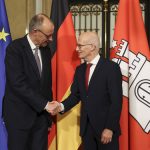 Merz zu Besuch in Hamburg Der Bundeskanler Friedrich Merz und der Bürgermeister Peter Tschentscher recihen sich die Hände. Im Hintergrund sind Flaggen aufgestellt.