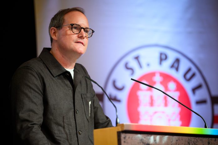 Mitgliederversammlung FC St. Pauli Der Präsident des FC St. Pauli, Oke Göttlich, steht an einem Rednerpult. Hinter ihm ist das Logo des Vereins zu sehen.
