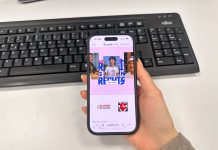 Rechtsextremer Onlineshop verliert vor Gericht Man sieht bei dem Blick über die Schulter einer Person den geöffneten Onlineshop Druck18.com auf einem Handy, vor einem Schreibtischhintergrund.