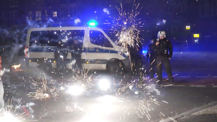 Böllerverbot Polizeibeamte stehen hinter explodierendem Feuerwerk.