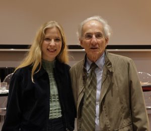 Ein Bild einer blonden Frau links mit einem älteren Herren rechts. Beide lächeln in die Kamera.