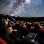 „MindSpace” – Der innere Kosmos Zu sehen sind Personen auf ihren Sitze im Sternensaal des Planetariums. Sie schauen mit 3D-Brillen auf die Projektionsfläche. Auf der Projektionsfläche der Kuppel ist ein Teil eines Universums zu sehen.