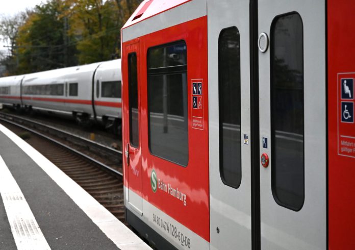 Auf dem Bild sieht man einen Teil des letzten Waggons einer S-Bahn. Dahinter fährt ein ICE vorbei.