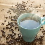 Zu günstiger Kaffee? Tchibo verklagt Aldi Süd Eine türkisfarbene Tasse Kaffee steht umgeben von Kaffeebohnen auf einem braunen Untergrund.