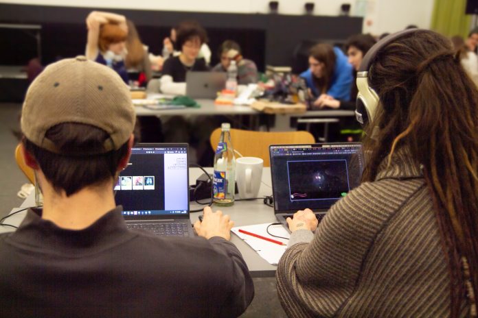 Zwei Personen sitzen am Laptop mit Kopfhörern und spielen Games