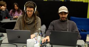 Zwei Personen sitzen am Laptop mit Kopfhörern und spielen Games