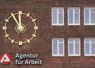 Hamburg hat bundesweit die dritthöchste Arbeitslosenquote Außenansicht auf ein Backsteingebäude mit einer goldenen Uhr und dem roten Logo der Agentur für Arbeit.