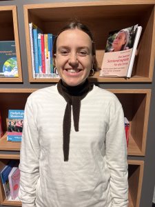 Eine junge Frau im Portrait, sie trägt einen Schal und einen weißen Pullover.