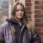 „Ich möchte einfach keine Mutter sein“ Eine junge Frau schaut in die Kamera. Sie hat lange braune Haare und steht vor einer Mauer. Links von ihr ist ein Innenhof im Hintergrund zu erkennen.