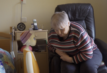 KI im Seniorenheim: Ein Roboter gegen Einsamkeit Ein KI-Roboter unterhält sich mit einer Bewohnerin eines Alten-und Pflegeheims. Die Bewohnerin sitzt auf einem schwarzen Ledersessel, der Roboter steht neben ihrem Bett.