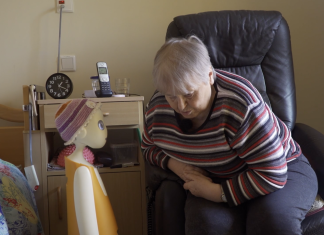 KI im Seniorenheim: Ein Roboter gegen Einsamkeit Ein KI-Roboter unterhält sich mit einer Bewohnerin eines Alten-und Pflegeheims. Die Bewohnerin sitzt auf einem schwarzen Ledersessel, der Roboter steht neben ihrem Bett.