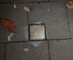 Messingstein auf dem Bürgersteig. Blätter liegen auf dem Boden.